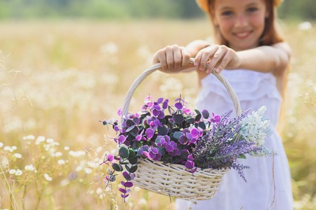 Happy girl is holding basket and stretching it to camera. She is standing on meadow and smilingの写真素材