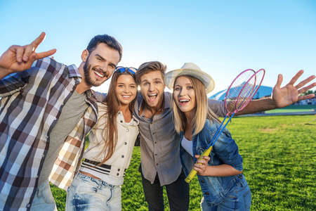cheerful friends smiling and looking into camera against blue sky