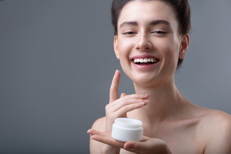 skin care concept, face of a young happy girl holding cream jarの写真素材