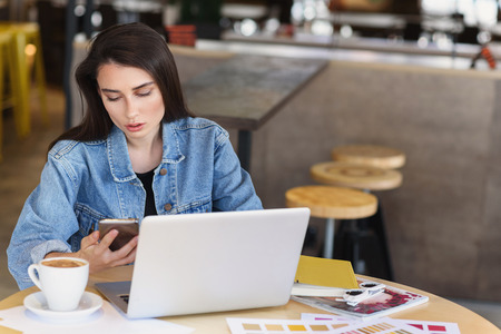 female freelancer looking into her smartphone in front of laptopの写真素材