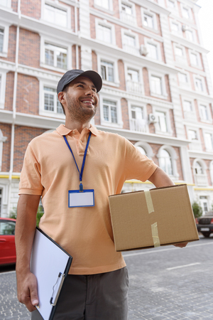 Always professional and on time. Cropped shot of cheerful young courier holding cardboard box while standing at entrance of apartmentの写真素材