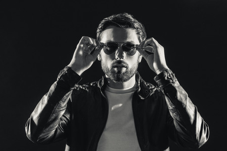 Passionate cool guy is standing and wearing his glasses with confidence. Black-and-white photo. Isolatedの写真素材