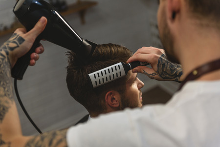 barber blow drying hair of a guy at hair salon, haircare conceptの写真素材