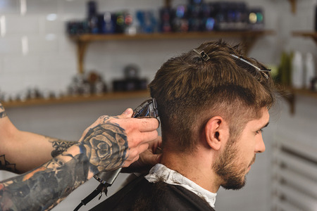 tattooed hands of a barber with clipper and client