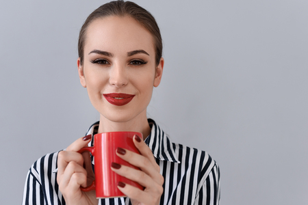 Happy young businesswoman is drinking coffee and relaxing. She is standing and smiling. Isolated and copy space in right sideの写真素材