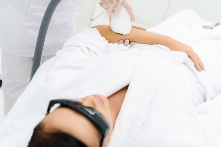 Young woman is getting ultrasound skin care treatment. She is lying with enjoyment. Beautician is pampering her arm by equipmentの写真素材