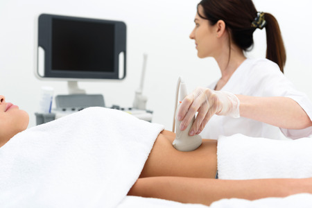 Experienced general practitioner is examining female abdomen by ultrasound equipment. She is sitting and looking at monitor with concentrationの写真素材