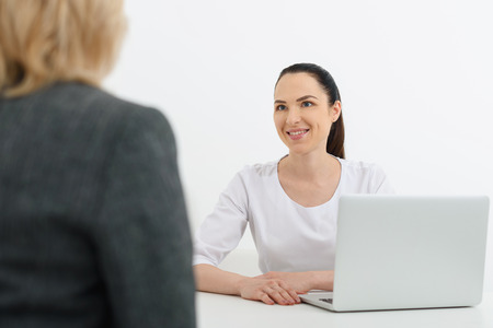 Friendly female beautician is talking with her patient and smiling. Women are sitting at desk in...