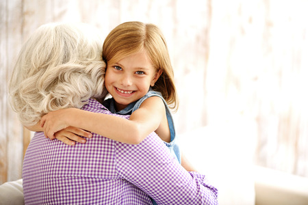 Happy girl is embracing mature woman with joy. She is looking at camera and smiling
