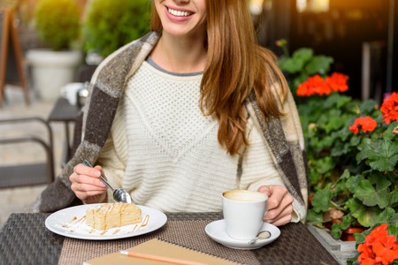 Happy young woman is enjoying breakfast in cafeteria. She is eating pastry and drinking coffee. Lady...