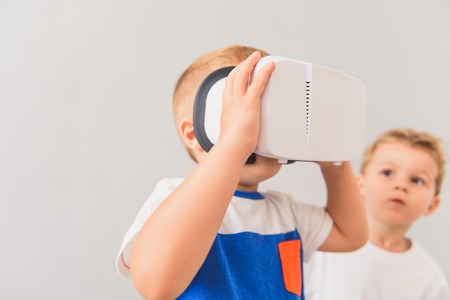 Cropped photo of little boy watching though virtual reality device with his friend on background...