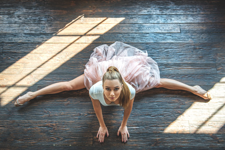 Her every line must be perfect. Top view of graceful ballerina sitting in cross splits on wooden floor and looking at cameraの写真素材