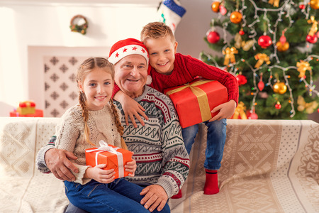 Friendly family is celebrating New Year together. Children are holding gifts and embracing their...