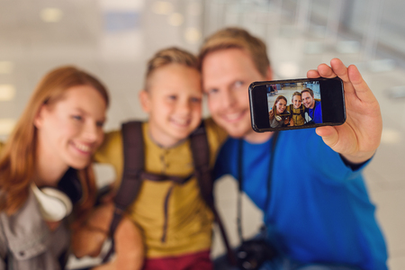 Say cheese. Close up of happy smiling family making selfie, using smartphone while staing at airportの写真素材
