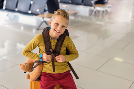Let is fly. Cropped photo of smiling little boy having fun while going on vacations trip with suitcase and backpack at airportの写真素材