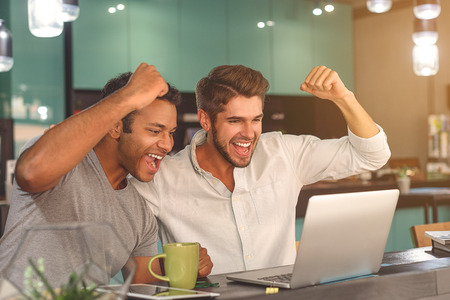 This is our victory. Shot of two male friends celebrating and looking at laptop while spending time in cafeの写真素材