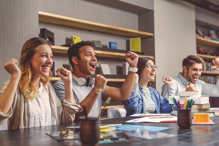 So glad to study together. Cropped shot of happy students sitting in row and enjoying success in classroom at deskの写真素材