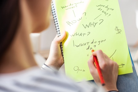 Close up of young woman writing her plans on paper with concentration. How, why and what questionsの写真素材