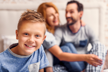 cute little boy looking at camera and smiling with happy parents in backgroundの写真素材