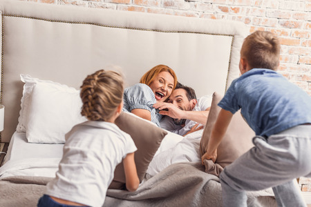 Best funny parents. cheerful smiling family having fun while playing pillow and lying in bedの写真素材