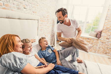 Smiling father holding pillow in hands and having fun with his family, spending time together