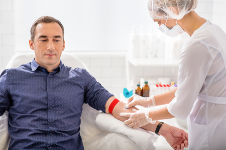 Skillful nurse is doing blood test for man in clinicの写真素材