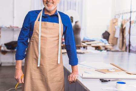 cheerful man in uniform and apron standing in front of workplaceの写真素材