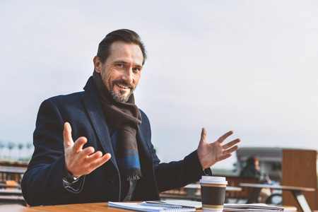 Joyful man is resting in cafe outdoors and gesturing with happiness. He is looking at camera and smilingの写真素材