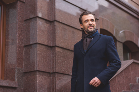 Joyful businessman is standing on staircase of building and smiling