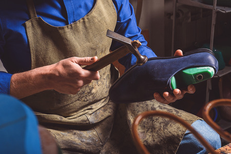 hammer in hands of a cobbler who holding a shoeの写真素材