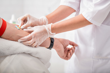 Close up of doctor arms sticking needle into male arm for blood samplingの写真素材