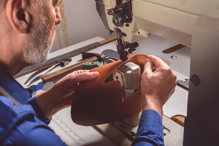 handyman operates an industrial sewing machine in a shoe factory, close up