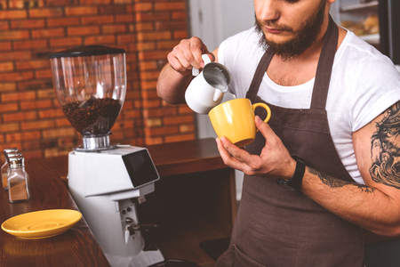Skillful barista is adding milk into cup of coffee with concentrationの写真素材