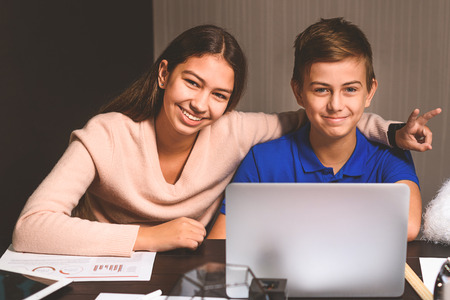 Teenagers are sitting in dayroom. Attentive boy is using computer, merry girl showing peace sign