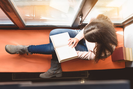 Top view of girl sitting on windowsill, she is holding volume at her kneesの写真素材