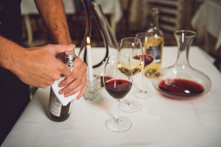 Man is opening bottle of white nectar. Many glassware on table