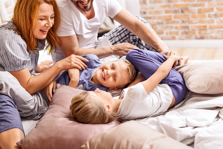 So much love. Close up of two little kids having fun with their parents, being at home in bed togetherの写真素材