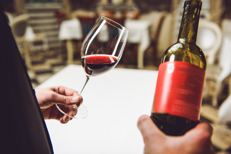 Man is holding glass with crimson nectar and bottle. Close upの写真素材