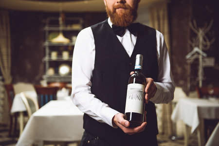 Waiter presenting burnished flask of beverage. Focus on wineの写真素材