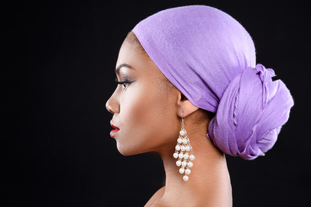 Peaceful mulatto girl is isolated on black background. She is wearing purple headscarf and earrings