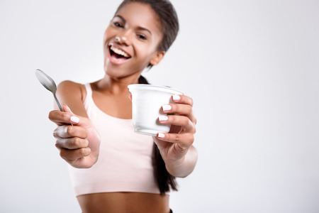 Stay healthy. Joyful girl is isolated on background. She is holding jar of dairy and a spoonの写真素材