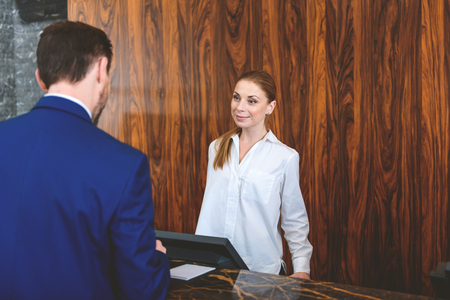 I hope you enjoy your stay. Friendly female receptionist looking at customer and smiling while standing behind reception deskの写真素材