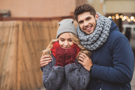 Happy loving couple is walking on street in cold weather. Man is hugging woman and laughing. Female eyes are closed with pleasureの写真素材