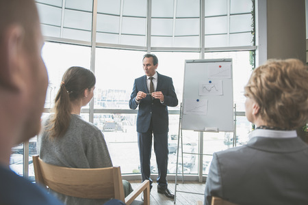 Serious boss is making an announcement to his employees. He is standing near the boardの写真素材