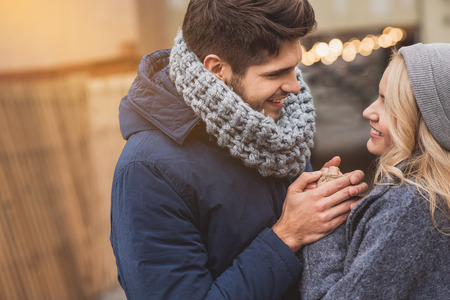 I love you. Joyful young man and woman are holding hands and smiling. They are standing on street in warm clothing. Lovers are looking at each other with tendernessの写真素材