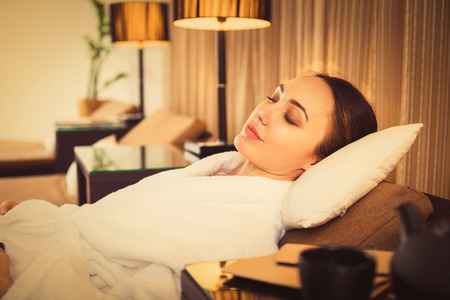 Calm young woman is resting after spa procedure. She is lying in white bathrobe with relaxationの写真素材