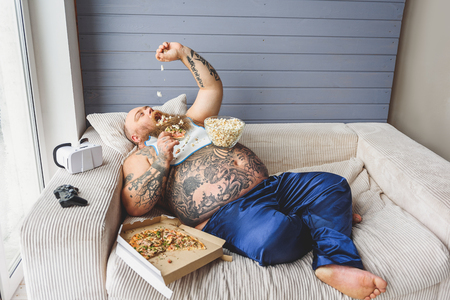 Lazy fat man eating unhealthy foodの写真素材