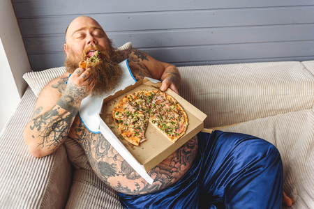 Male heavy eater biting unhealthy foodの写真素材