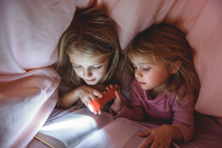 Pretty kids reading story under quiltの写真素材
