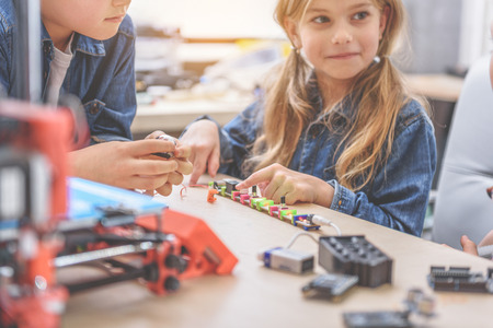 Happy girl is sitting beside boy near wooden desk, full of different equipment. She looking asideの写真素材